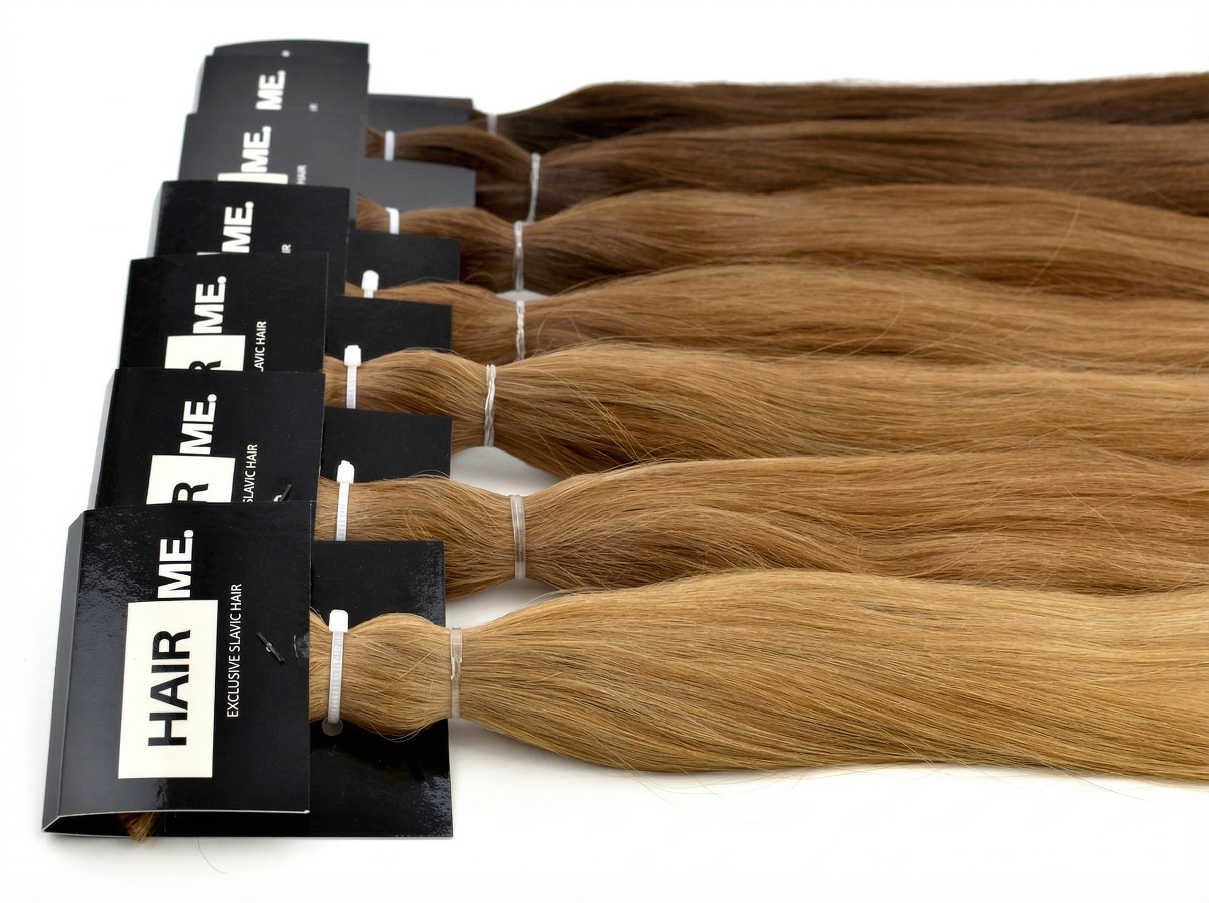 Zestaw kilku pasm z&nbsp;włosów naturalnych w&nbsp;różnych odcieniach blondu i&nbsp;jasnego brązu ułożonych na&nbsp;białym tle.