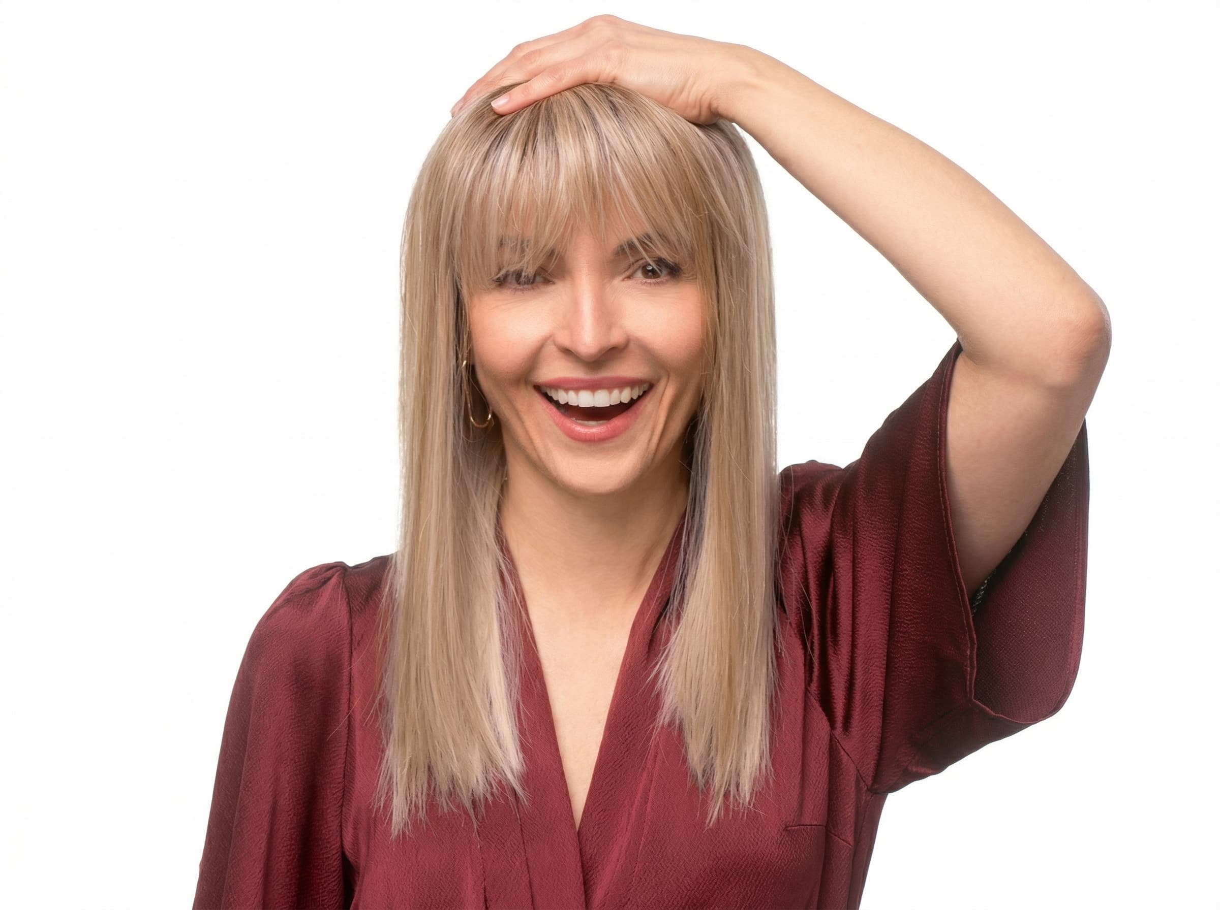 Uśmiechnięta kobieta poprawiająca włosy, prezentująca stabilność długiej, jasnej peruki medycznej z&nbsp;prostą grzywką z&nbsp;salonu Rokoko.