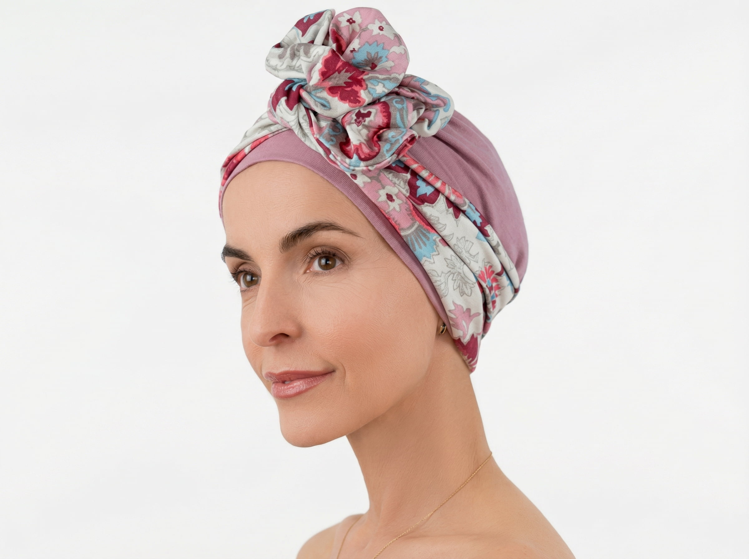 Kobieta w&nbsp;jasnym topie nosi turban w&nbsp;kolorze pudrowego różu z&nbsp;dekoracyjnym węzłem i&nbsp;wzorzystym panelem z&nbsp;przodu.