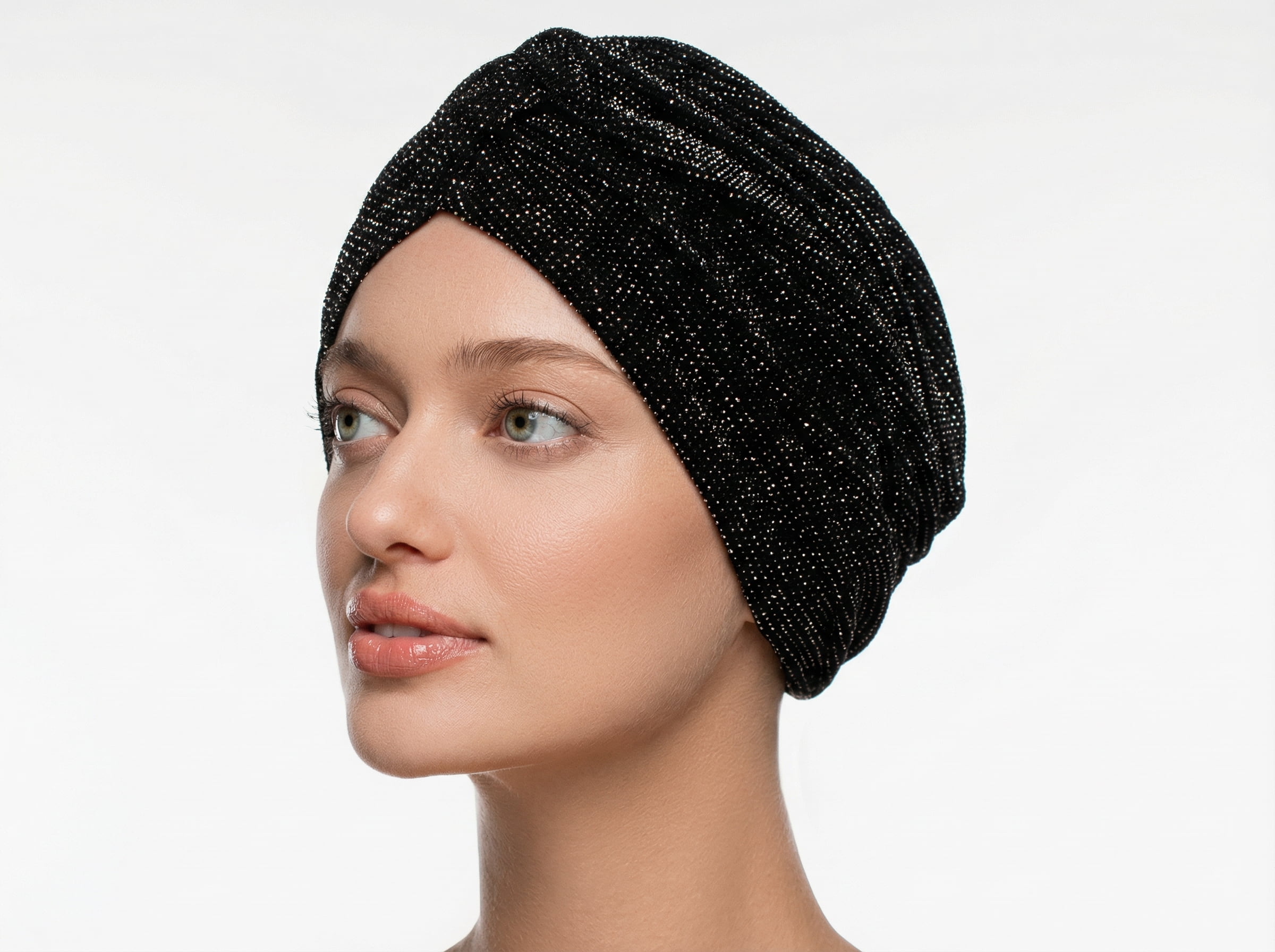 Kobieta w&nbsp;czarnym, lekko połyskującym turbanie z&nbsp;delikatną fakturą, widziana z&nbsp;profilu na&nbsp;białym tle.