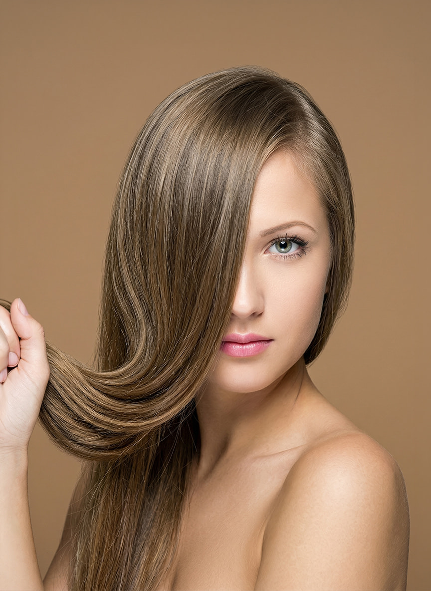 Kobieta z&nbsp;gęstymi, długimi włosami w&nbsp;odcieniu ciemnego blondu, prezentująca pasmo włosów. Efekt zastosowania włókien zagęszczających z&nbsp;oferty Rokoko na&nbsp;beżowym tle.