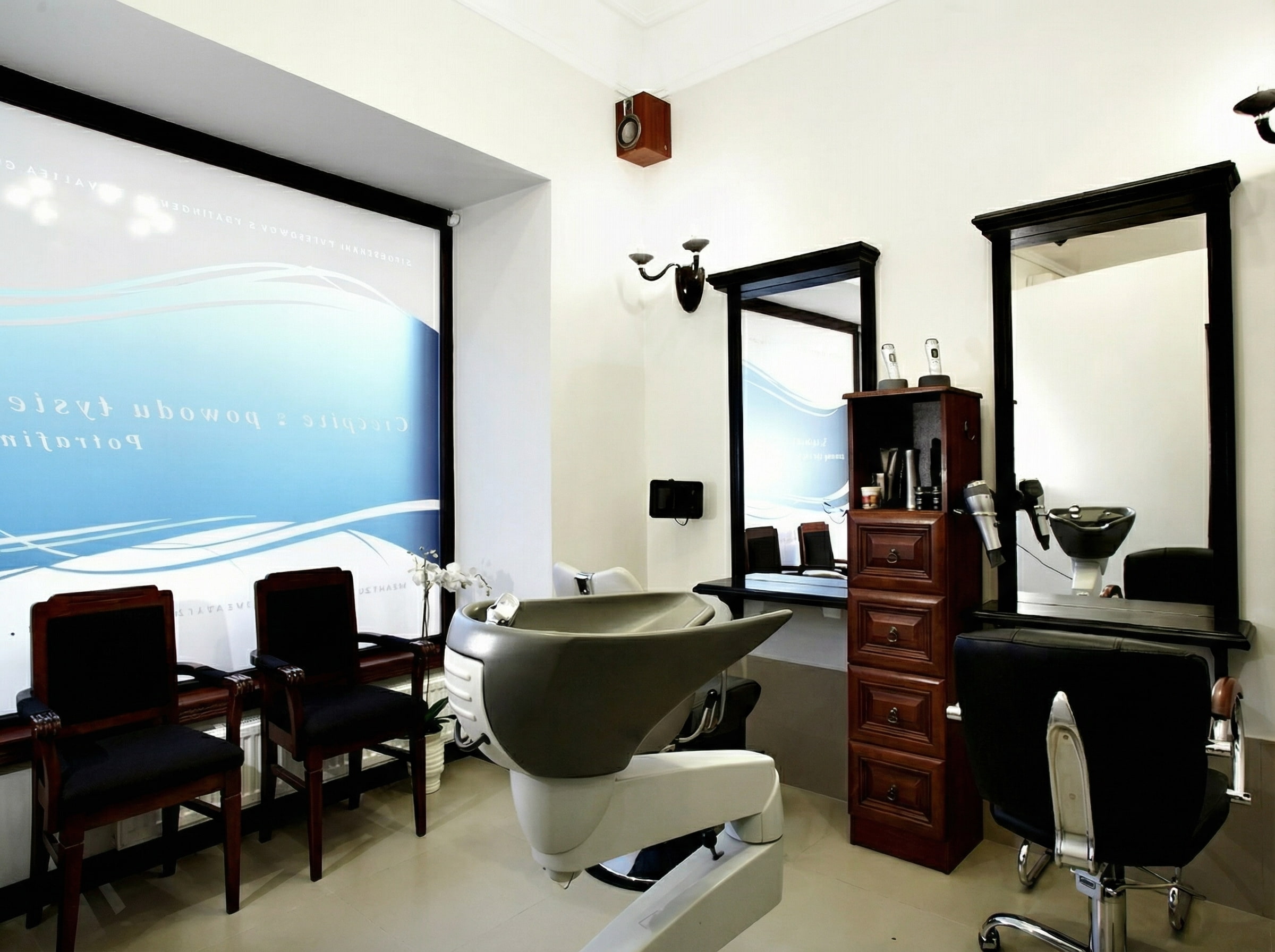 Jasne, nowoczesne wnętrze salonu fryzjerskiego Rokoko z&nbsp;widoczną myjką do&nbsp;włosów, dużymi lustrami oraz eleganckimi, czarnymi fotelami do&nbsp;stylizacji.