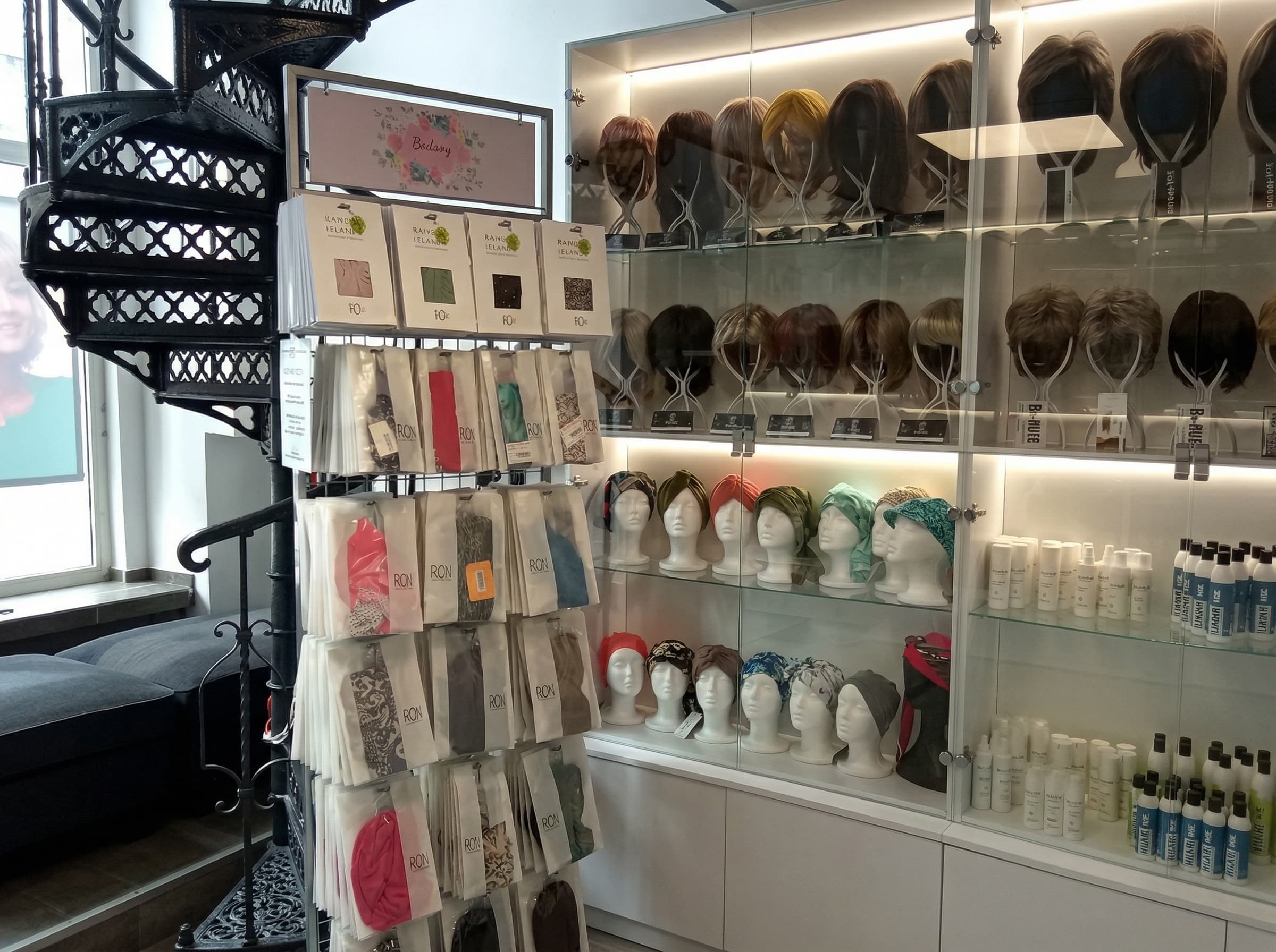 Jasne wnętrze sklepu Rokoko w&nbsp;Częstochowie z&nbsp;widocznym stojakiem pełnym turbanów, półkami z&nbsp;kosmetykami oraz podświetlaną witryną z&nbsp;perukami na&nbsp;manekinach.